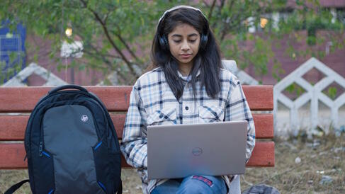 Female student sitting on a bench typing into a laptop